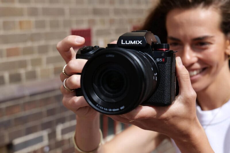 Пользователь с улыбкой держит камеру Panasonic Lumix S5 II у лица, готовясь сделать снимок