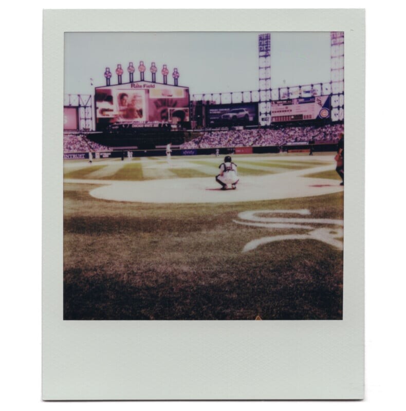 Снимок бейсбольной игры на стадионе, на котором показан отбивающий игрок, ловец и большой табло на заднем фоне.