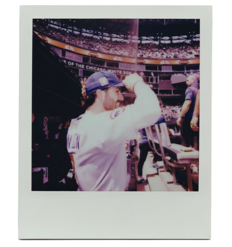 Мужчина в бейсбольной форме улыбается и приветствует болельщиков на стадионе.