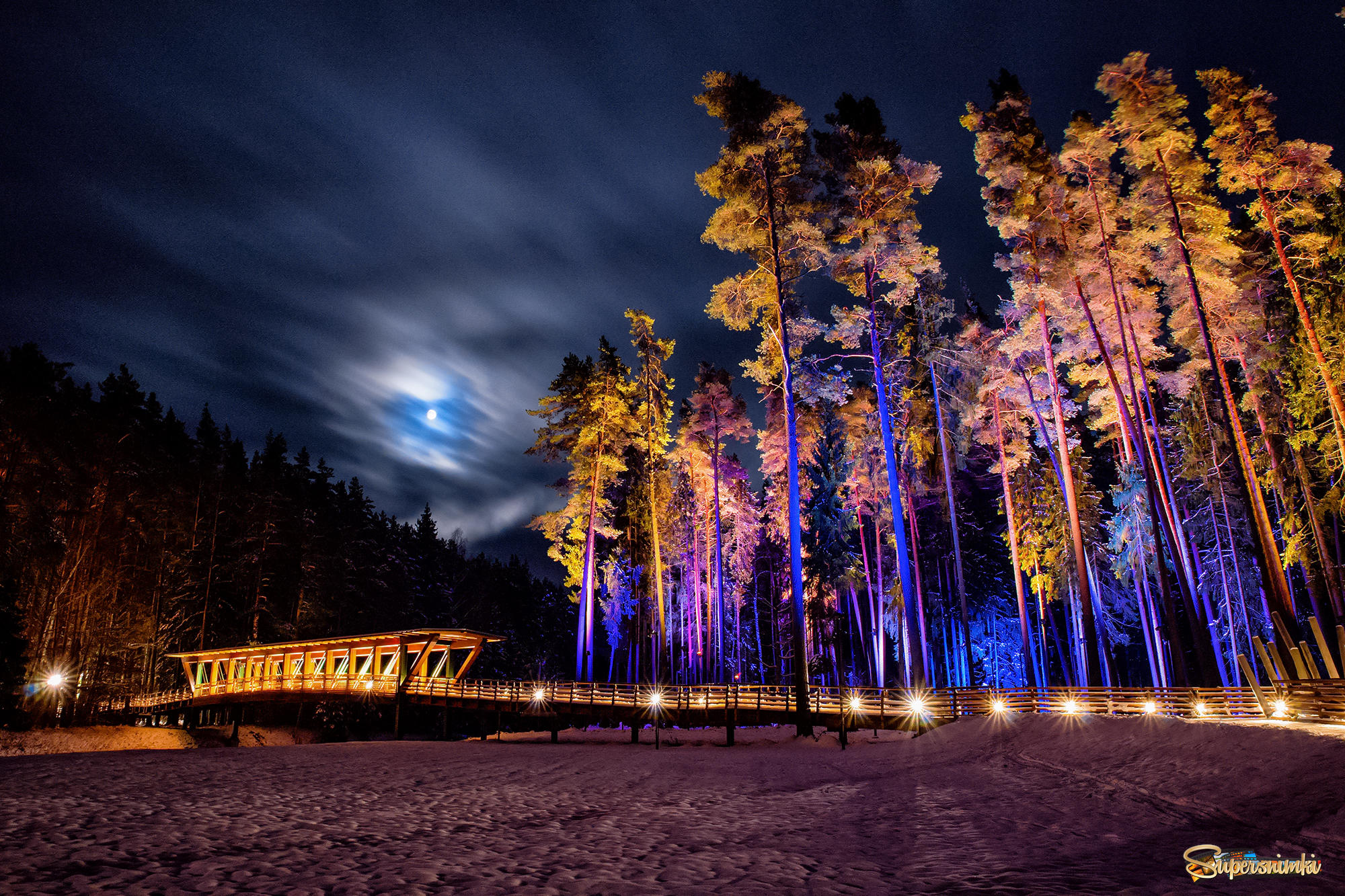 Облачная луна в зимнем лесу над снежным мостом.