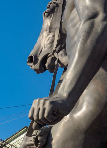 A bronze figure of a large size monument of a young man with a horse stands on a street of the city of St. Petersburg.